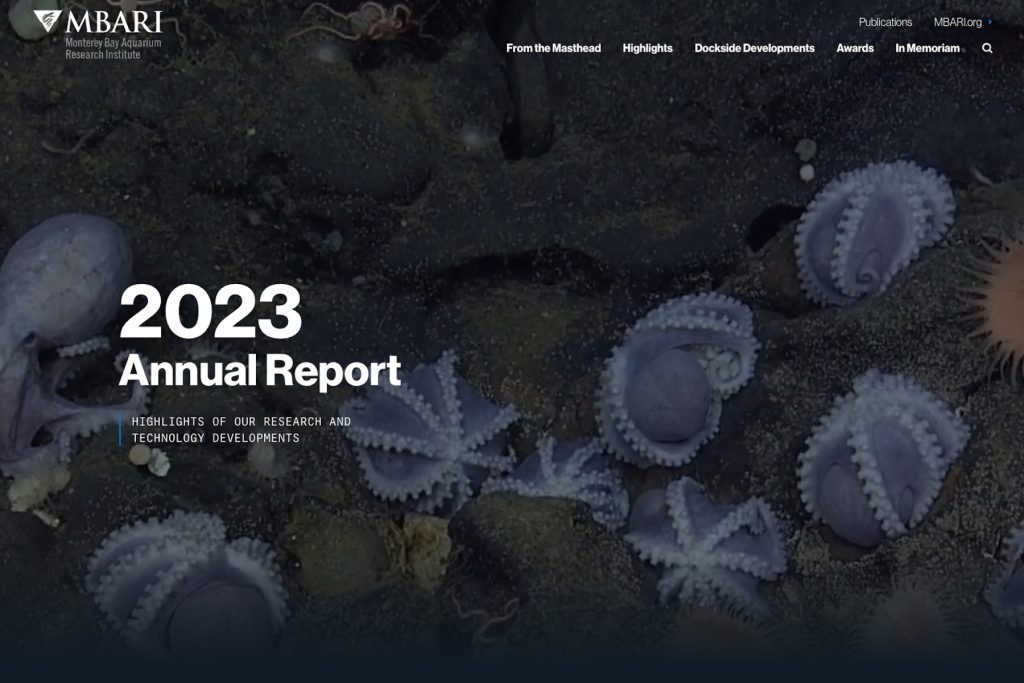 A screenshot of the main landing page for MBARI’s 2023 Annual Report. At the top left is MBARI’s gulper eel logo and the full name “Monterey Bay Aquarium Research Institute” in white. At the top right is white text reading “Publications” and “MBARI.org” with a row of bold white text below reading “From the Masthead,” “Highlights,” “Dockside Developments,” “Awards,” and “In Memoriam” and a white magnifying glass search icon. In the center of the page is a frame grab from a video of purple deep-sea octopus nesting between greenish-black rocky boulders and bold white text reading “2023 Annual Report” and a bright blue vertical bar next to smaller white text reading “Highlights of our research and technology developments” in all caps.