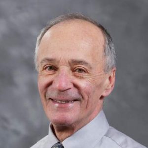 A headshot shows a former member of the MBARI Board of Directors with receding gray hair wearing a gray shirt and tie. The background is a textured gray screen.